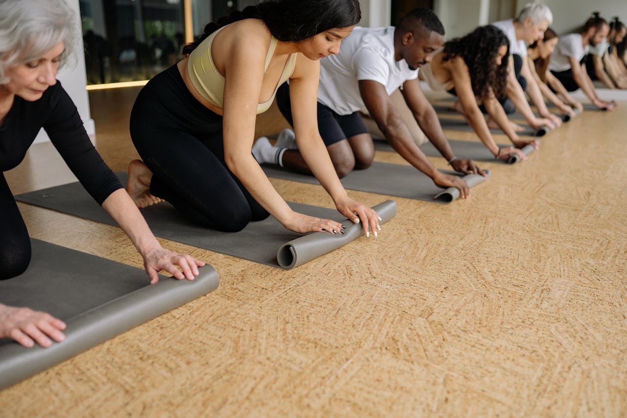 A diverse group of adults rolling yoga mats in a studio before practice, promoting fitness and wellbeing.